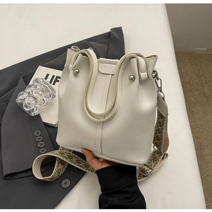 Detail der cremefarbenen Beuteltasche mit Boho-Stickerei-Gurt und glatter Ledertextur