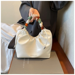 Close-up of white ruched bucket bag with colorful beaded handle and logo detail