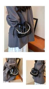 Detail of glossy black patent leather drawstring bucket bag with pearl chain strap