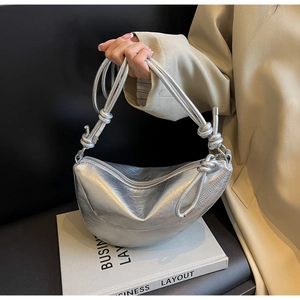 Detail of silver croissant bag featuring metallic pleated texture and knot shoulder strap