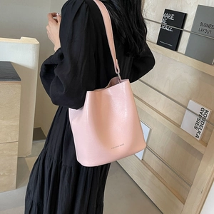 Sac seau minimaliste rose en cuir à motif litchi porté à l'épaule sur un mannequin