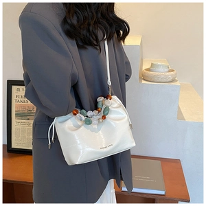 Detail of white pleated cloud bag featuring colorful bead handle and crossbody strap