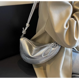 Detail of silver crescent bag with wrinkled texture finish and decorative knot on shoulder strap