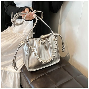 Close-up of metallic silver drawstring bucket bag with shiny beaded handle and slim strap
