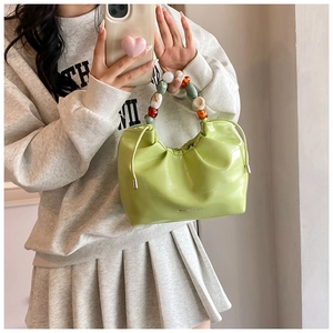 Detail of lime green ruched bucket bag with vibrant acrylic beaded handle and glossy texture