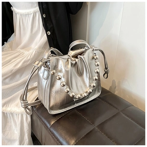 Close-up of silver metallic bucket bag with decorative beaded handle and knotted strap details