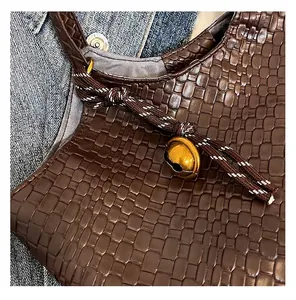 Détail d'un cabas tressé marron avec nœud décoratif et breloque clochette dorée sphérique