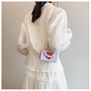 Detalle de mini bolso lavanda con diseño de corazón, asa de perlas y cadena chic