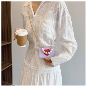 Detalle de mini bolso morado con corazón, asa de perlas y cadena dorada