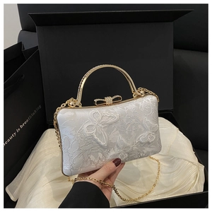 Close-up of white lace evening bag featuring golden butterfly embroidery and bow clasp
