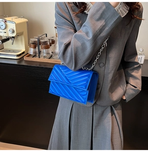 Detail der leuchtend blauen gesteppten PU-Lederhandtasche mit silberner Kette am Modell