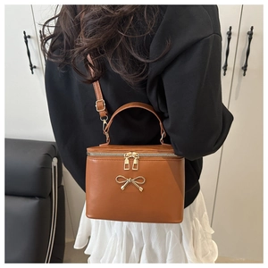 Detail der karamellbraunen Koffer-Tasche mit goldener Schleife und strukturierter PU-Haut