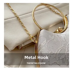Close-up of golden metal handle and ball clasp detail on elegant beige lace clutch bag
