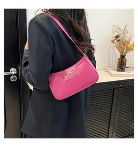 Detail of rose pink crescent shoulder bag with golden bow ornament on a black blazer
