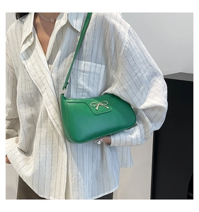 Detail of green crescent underarm bag with gold bow clasp on a striped shirt model