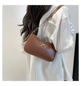 Detail of brown leather baguette bag with silver bow accent on white stripe shirt