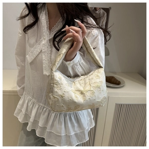 Gros plan sur la broderie papillon dorée d'un sac à bandoulière en tissu blanc cassé