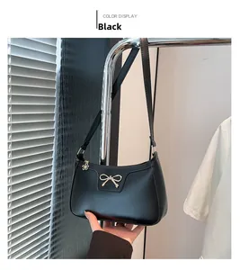 Detail of minimalist black leather shoulder bag with gold bow and petal zipper charm
