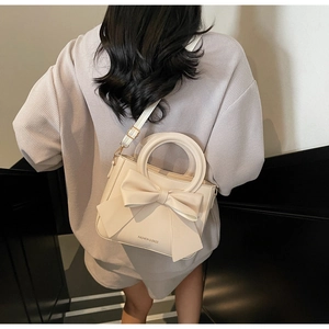 Detail showing bow design and metal buckles on a cream bucket bag worn by a model