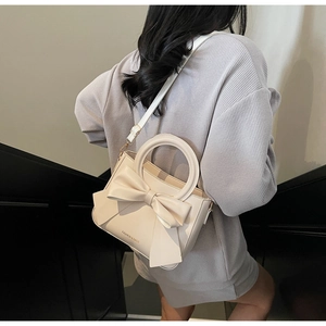 Close-up of cream-white bucket bag featuring a large bow and adjustable strap detail