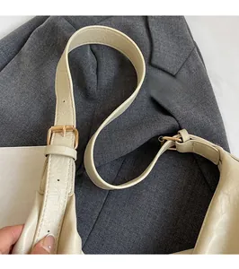 Detail of adjustable leather strap and golden metal buckle on beige crossbody tote bag
