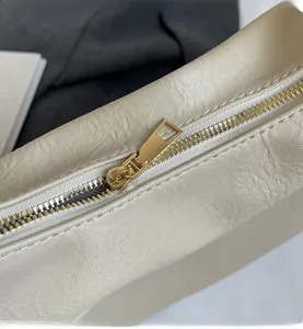 Macro shot of smooth gold metal zipper and premium leather texture on the cream tote bag