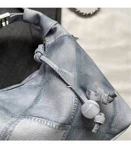 Detail of light blue denim dumpling bag featuring geometric stitching and marble bead charm