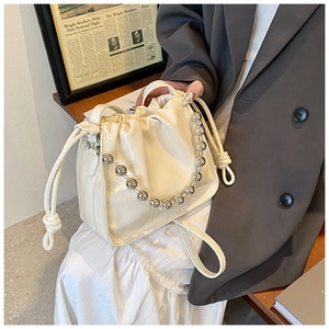 Detail of cream drawstring bucket bag with crocodile texture and metallic bead handle
