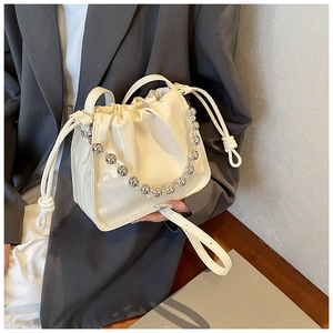 Detail of cream drawstring bucket bag with glossy embossed texture and pearl bead handle