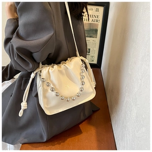 Detail of a creamy white pleated drawstring bucket bag with silver bead chain strap