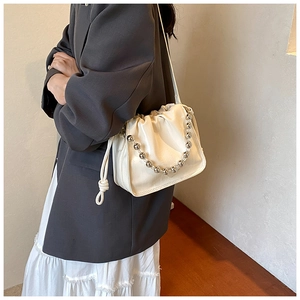 Detail of cream drawstring bucket bag with silver ball chain and knotted tassels on a model