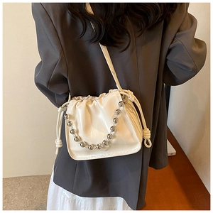 Close-up of beige drawstring bucket bag with textured leather and metal bead chain