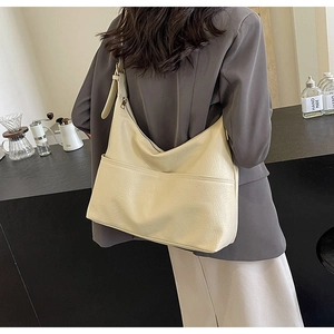 Close-up of cream-white hobo tote bag with front pocket shown on a model's shoulder