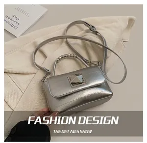 Détail d'un sac carré argenté avec grand fermoir pyramide et poignée en perles