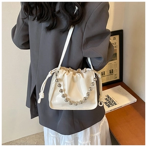 Detail of white drawstring bucket bag with silver beaded chain and glossy leather finish