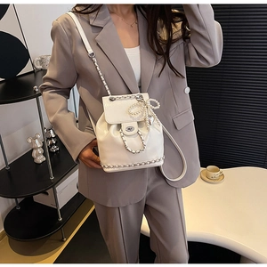 Detail van witte mini rugzak met glanzende afwerking, ketting en parel strik hanger
