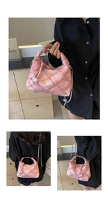 Detail of pink quilted hobo bag with chain strap and tassel charm on a wooden stand