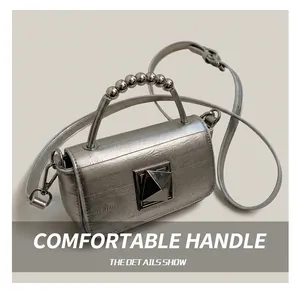 Détail du sac à main en cuir argenté avec poignée perlée et fermoir métallique géométrique