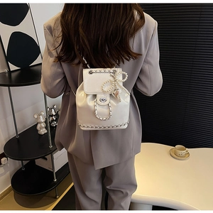 Detail van witte mini rugzak met parelstrik en zilveren ketting gedragen door model