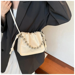 Detail of a creamy white drawstring bucket bag featuring a glossy finish and silver chain