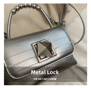 Détail d'un sac argenté avec un grand fermoir carré et une poignée à perles métalliques
