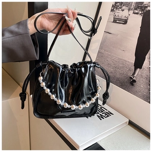 Detail of black glossy drawstring bucket bag featuring silver bead chain and metal logo