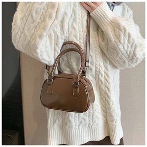 Borsa bowling marrone in pelle lucida indossata da una modella con un maglione bianco