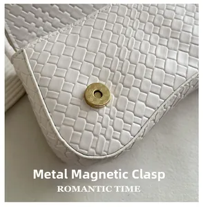 Close-up of golden magnetic buckle on white woven leather minimalist baguette bag