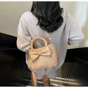 Detail of beige bucket bag with large bow decoration worn crossbody on a casual outfit