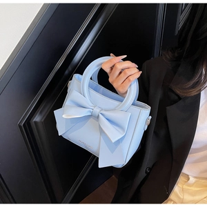 Detail of light blue bucket bag with a large bow held by a model in a black suit