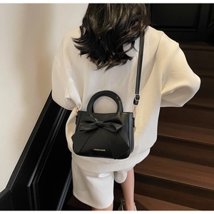 Detail of a black leather bucket bag with a large bow and gold lettering on a model