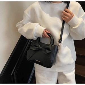 Detail view of black bucket bag with large bow and fashion text on white sweatshirt