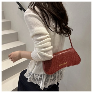 Detail of brick red woven baguette bag with fashion lettering on smooth faux leather
