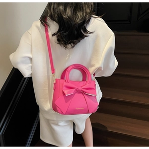 Close-up of bright pink bucket bag featuring large bow design and fashion slogan